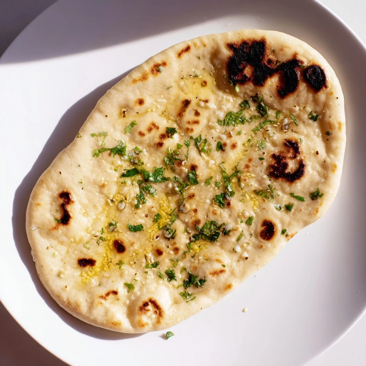 Image of soft, pillowy Homemade Garlic Naan Bread dotted with savory brown spots, just out of the pan.