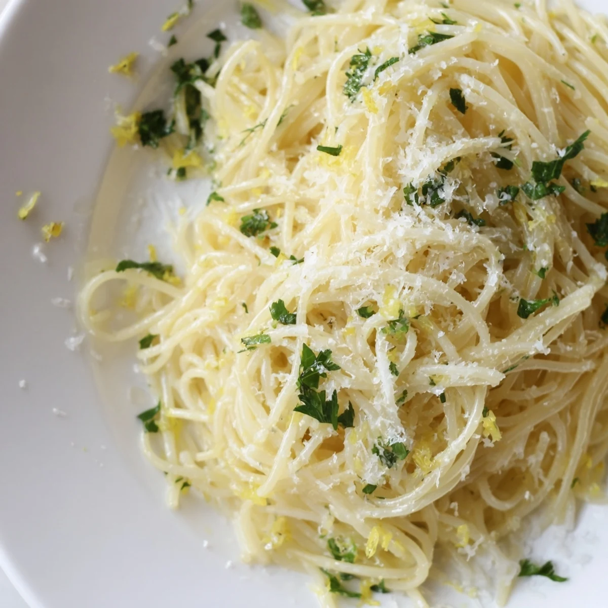 A close-up of Lemon Butter Pasta Light, showcasing silky strands of capellini coated in a glossy lemon-butter sauce and fresh parsley garnish.  