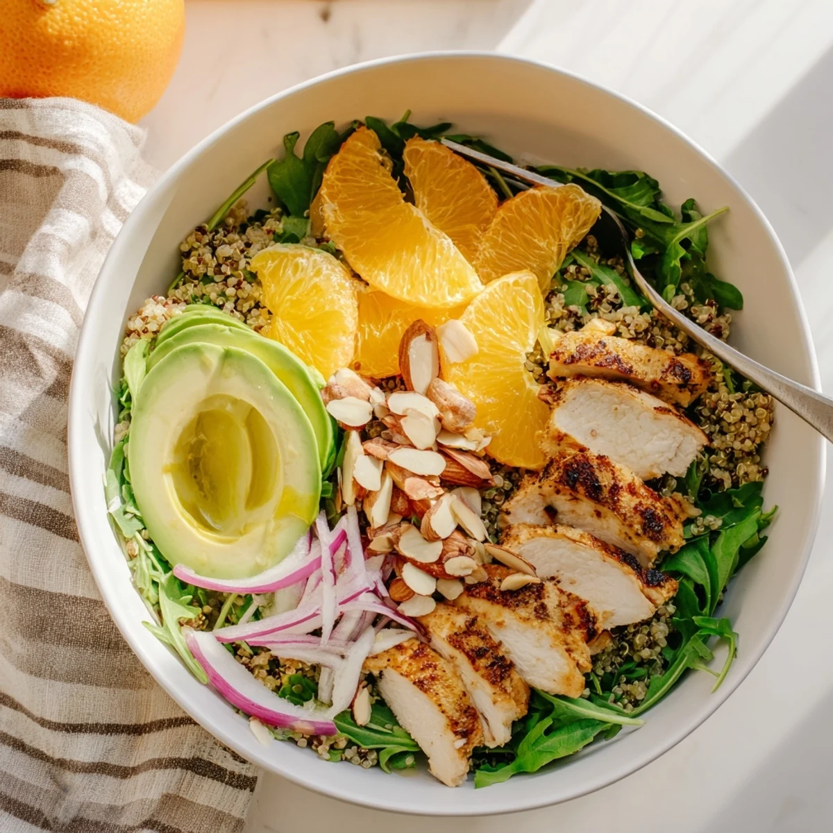 Sliced herb-marinated grilled chicken rests atop a vibrant bowl of mixed greens, fluffy quinoa, and creamy avocado for this Citrus Herb Chicken Salad Bowl.