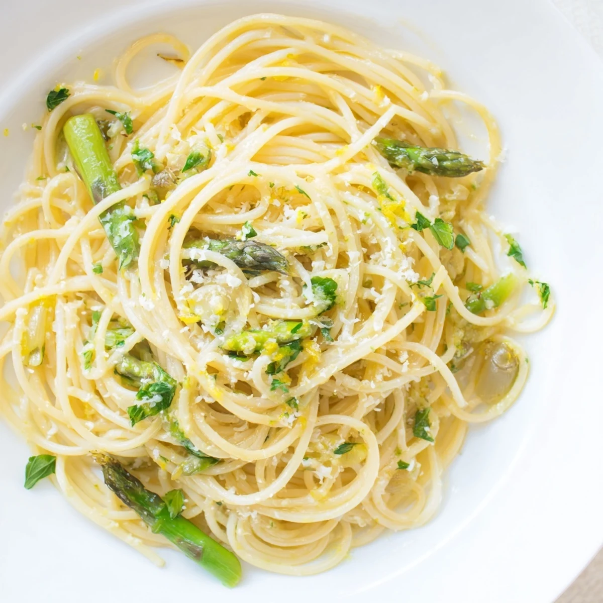 A close-up of Roasted Garlic & Asparagus Pasta with glistening olive oil, lemon zest, and fresh parsley over strands of spaghetti.