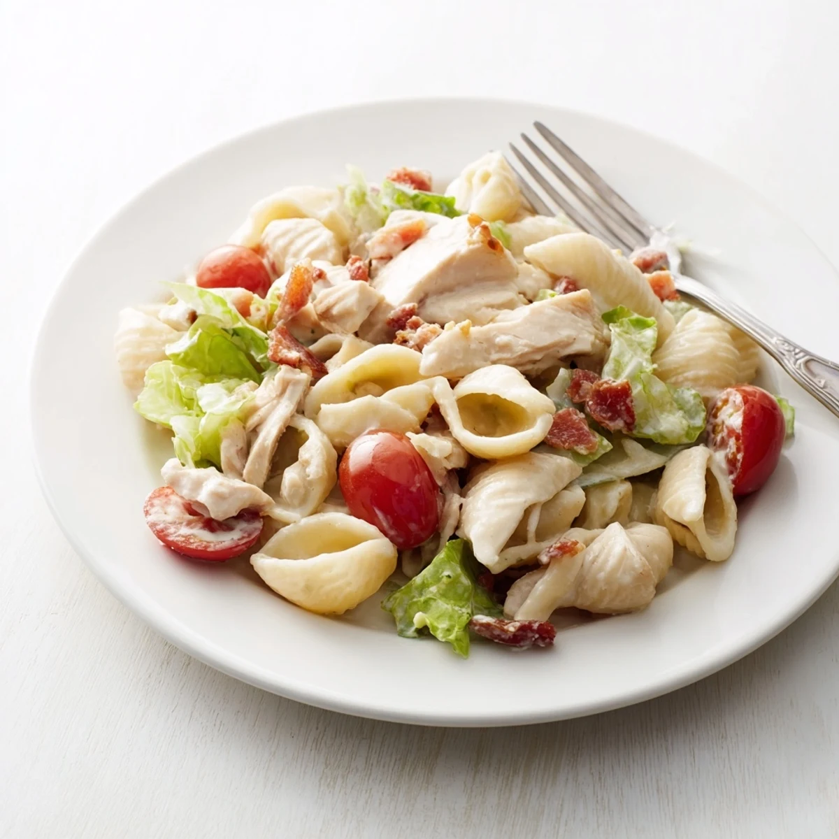 BLT Chicken Pasta Salad in a white bowl features creamy dressing, tender pasta shells, grilled chicken, crisp lettuce, and juicy tomatoes.  