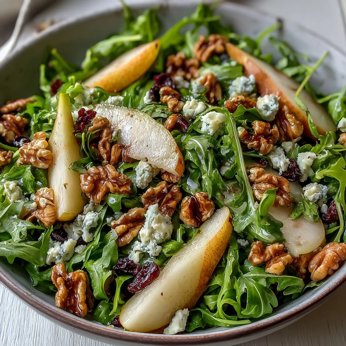Arugula and Pear Bowl salad garnished with goat cheese and pecans, drizzled with balsamic dressing in a rustic white bowl.