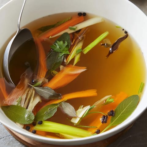 A fine-mesh sieve strains the rich Vegetable Broth from Scraps into a clear glass bowl.