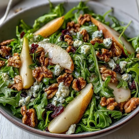 Arugula and Pear Bowl salad garnished with goat cheese and pecans, drizzled with balsamic dressing in a rustic white bowl.