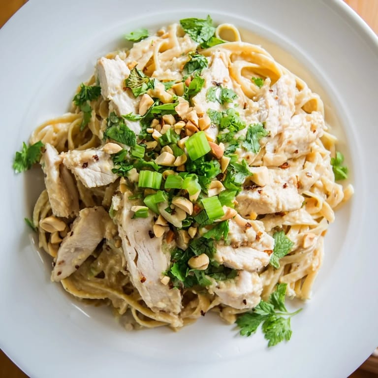 A close-up of delicious Thai Peanut Chicken Pasta garnished with peanuts and green onions, served warm.