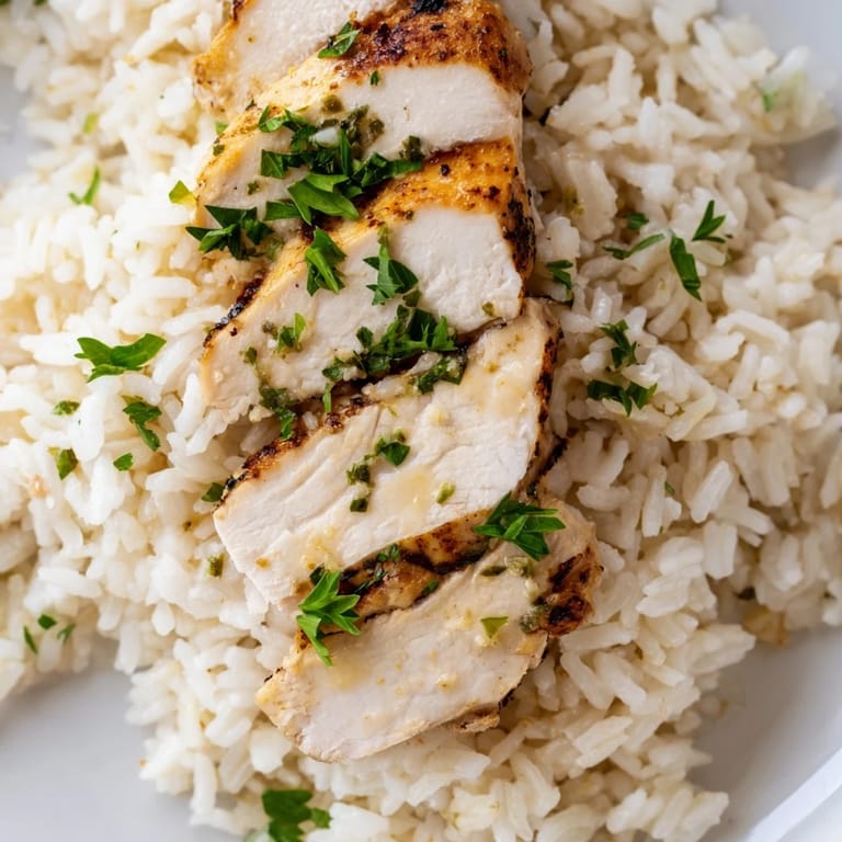 A close-up of succulent chicken breast atop tender rice infused with rich garlic butter and finely chopped onion.