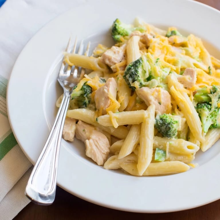 Family-style Chicken Broccoli Cheddar Pasta in a white dish, garnished with extra cheddar and a side salad for a comforting dinner.