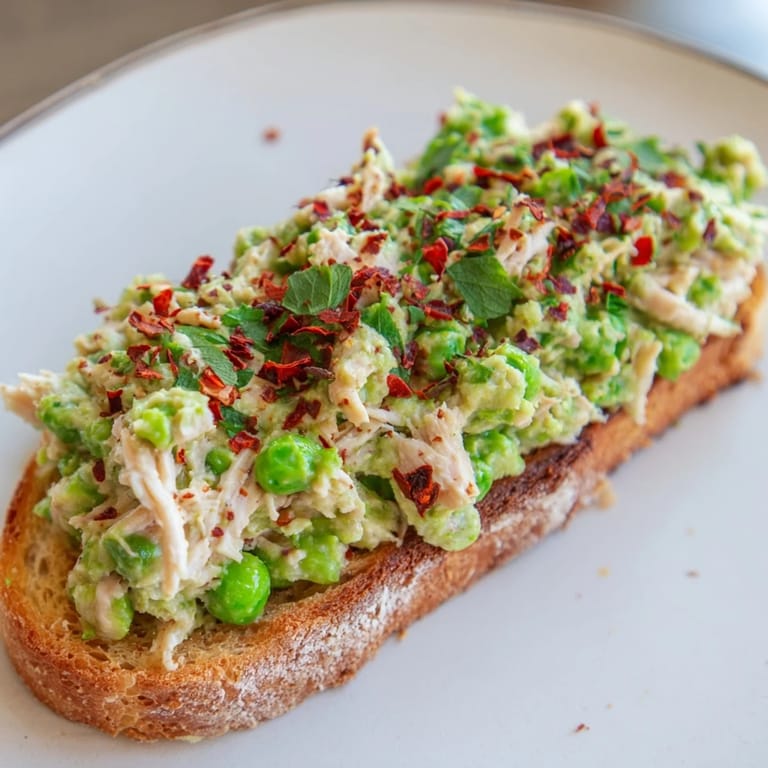 Serve this protein-rich Smashed Pea & Chicken Toast warm, featuring a chunky pea mash and spicy chili flakes on crispy rustic bread.