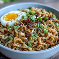 Close-up of glossy garlic butter ramen, garnished with green onions and a soft-boiled egg.